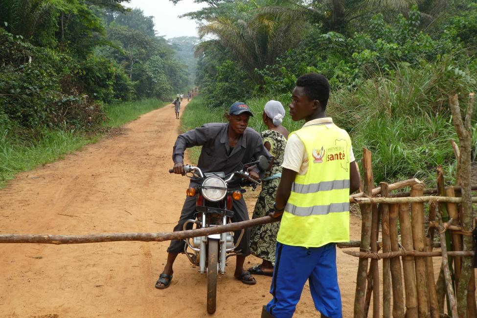 A health officer on the outskirts of Itipo prepares to open a barrier for a motorbike driver who has undergone screening . Photo: IOM