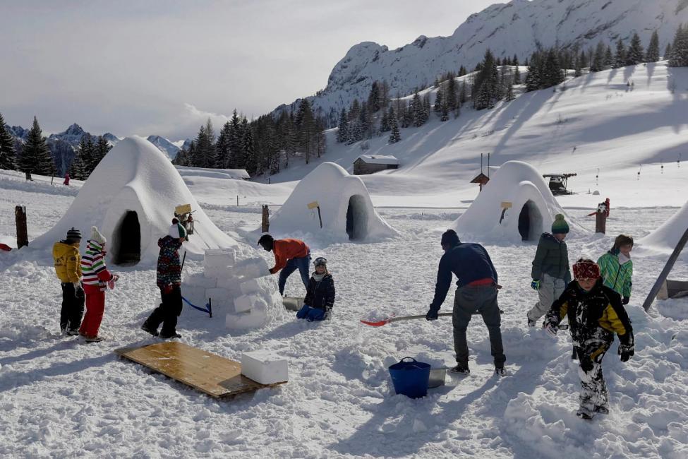 In this photo taken on Friday, Feb. 2, 2018, Omar Kanteh, of Gambia, with red fleece at center, and Moussa Sissoki, of Mali, holding a shovel at center right, are surrounded by children as they build igloos in San Simone di Valleve, near Bergamo, northern Italy. Migrants from African nations far from the frozen north picked up the art of igloo making to help a local restaurant owner realize a project to lure tourists back to this dying mountain resort. (Luca Bruno/Associated Press)
